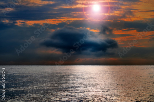 A stormy sunset over the dark sea. The bright rays of the sun through the gloomy clouds, the reflection of the sun in the water.