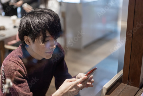 カフェの窓辺でスマートフォンを操作する20代男性