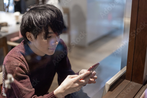 カフェの窓辺でスマートフォンを操作する20代男性