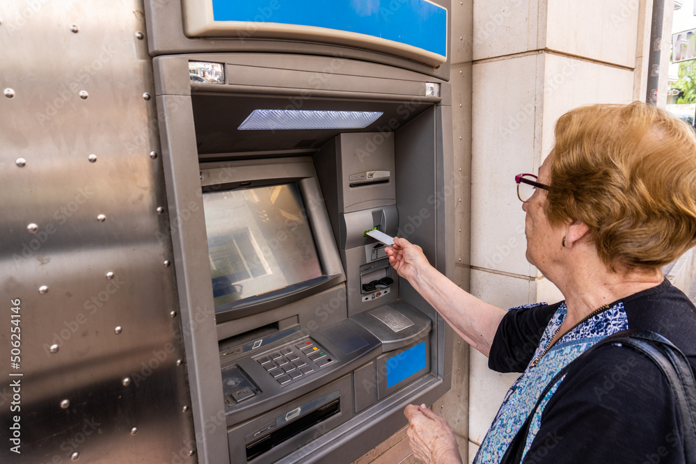 Elderly woman using an ATM in the street - obrazy, fototapety, plakaty 