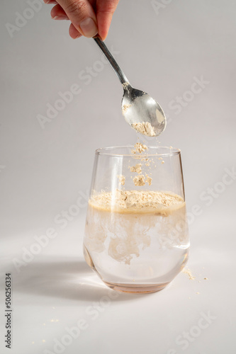 Woman pours collagen powder or protein in a glass of water on a beige background. A healthy and anti aging supplement. Copy space photo