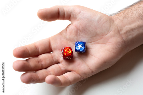 On the man's palm are two dice with images of the symbols of the hammer and sickle and white star. The concept of the confrontation between the two ideologies of communism and capitalism.
