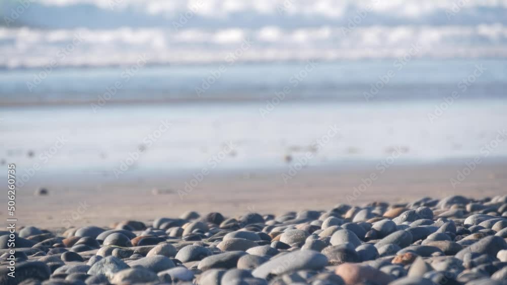 Pebble rocks on sandy beach by ocean sea water waves, round smooth stones or boulders low angle view in soft focus. California coast vacations aesthetic, USA. Seascape natural background with bokeh. Pebble rocks on sandy beach by ocean sea water waves, round smooth stones or boulders low angle view in soft focus. California coast vacations aesthetic, USA. Seascape natural background with bokeh.