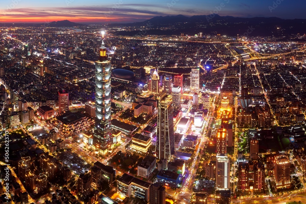 Aerial view of Downtown Taipei at dusk, the vibrant capital city of Taiwan, with 101 Tower standing out amid skyscrapers in Xinyi Commercial District and city lights dazzling under golden twilight sky