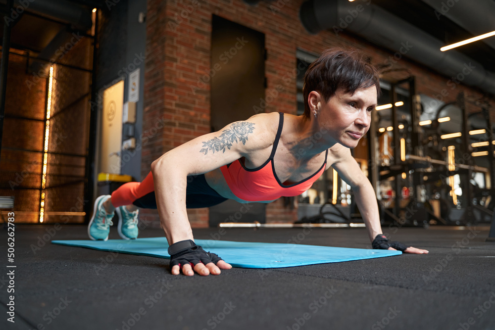 Fototapeta premium Muscular woman performing push-up on gym floor