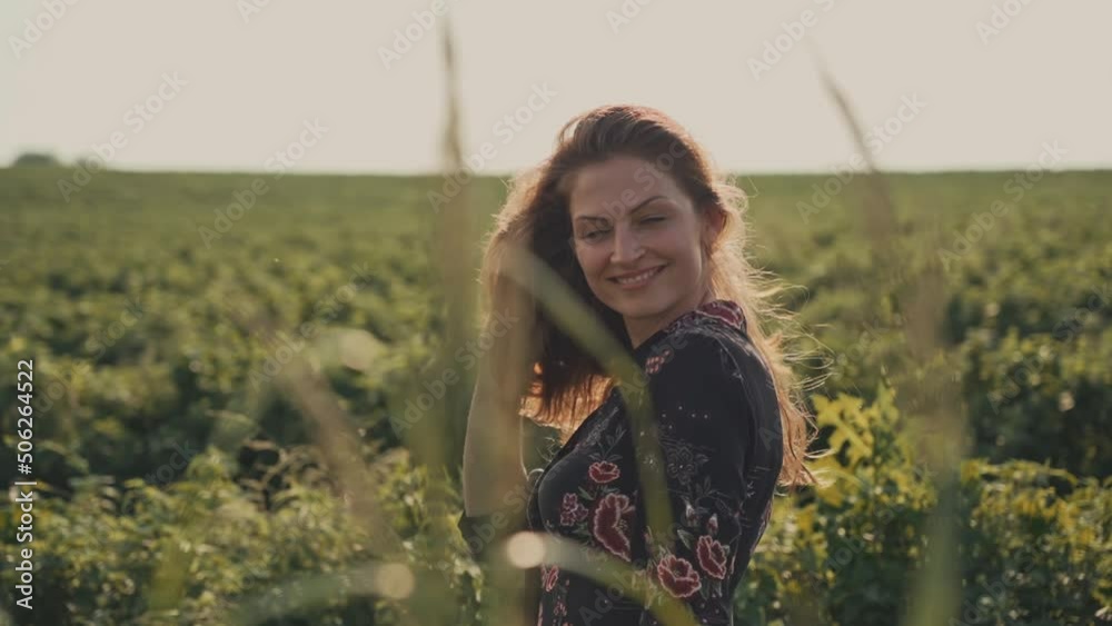 Young happy woman with flowing hair and blue eyes in a summer dress in the field, woman raises her head, smiling and looking at camera. Young happy woman with flowing hair and blue eyes in a summer dress in the field, woman raises her head, smiling and looking at camera.