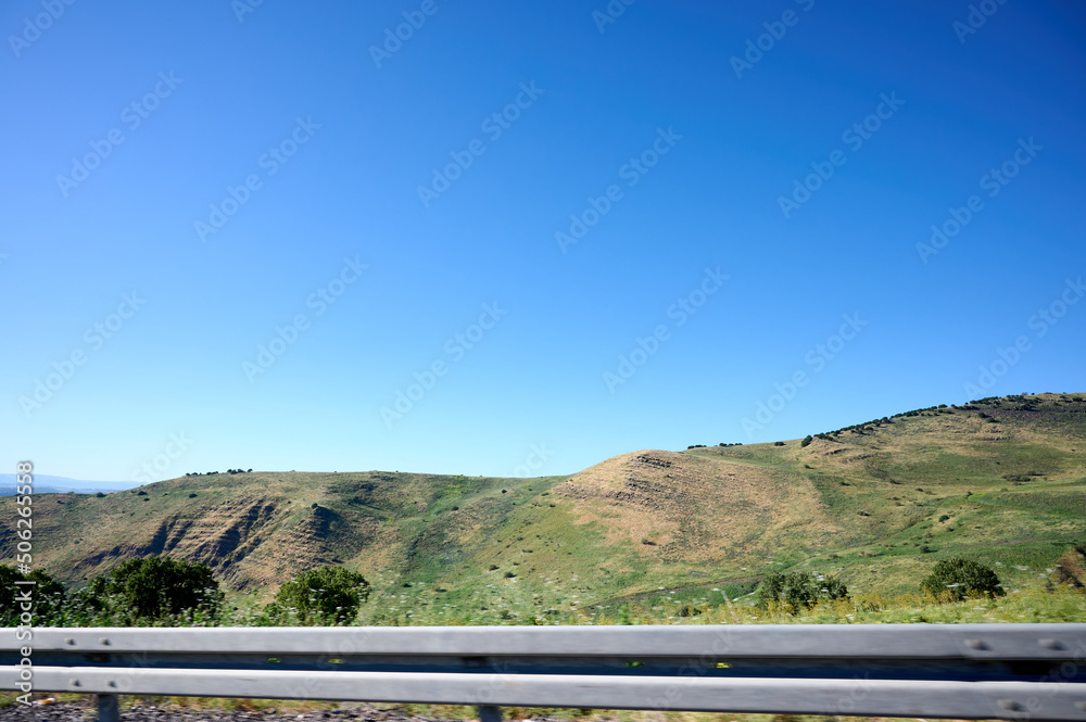 Photo from the window of a car driving on the highway. Landscape of a green plain with hills and mountains in the distance. Photo from the window of a car driving on the highway. Landscape of a green plain with hills and mountains in the distance.