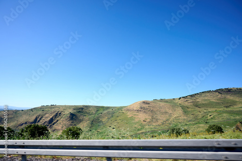 Photo from the window of a car driving on the highway. Landscape of a green plain with hills and mountains in the distance.