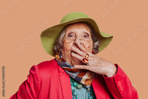 Surprise astonished elderly grandmother. Close up portrait of white-skin old woman looking surprised in full disbelief with open mouth and raised hand.