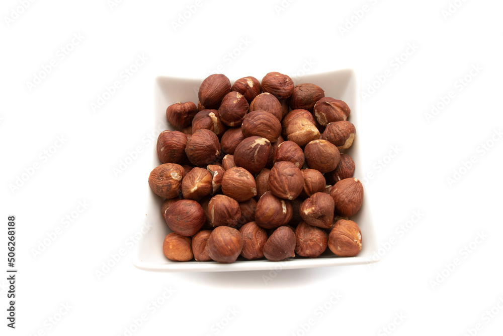 A white bowl with hazelnuts, isolated on white background.Hazelnut is the nut-like fruit of the common hazel, Corylus avellana. Etymologically it comes from the Latin nux abellana. A white bowl with hazelnuts, isolated on white background.Hazelnut is the nut-like fruit of the common hazel, Corylus avellana. Etymologically it comes from the Latin nux abellana.