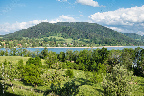 Landscape shot of Lake Tegernsee, Bavaria, Germany on a sunny day with some clouds in the background of a small hill.  photo