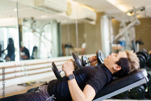 Active Asian sportsman doing a weight exercise in a gym - fitness by lifting up a dumbbell.