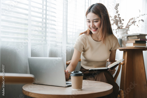 Smiling Asian woman holding a note in hand and standing near window Startup business Asian woman online SMEs Telemarketing