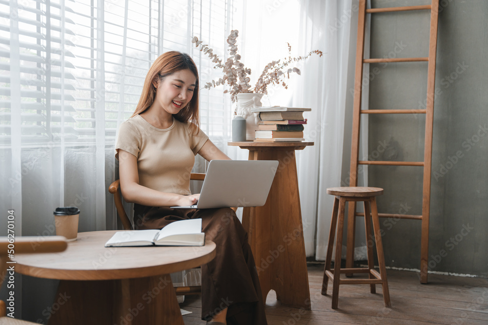 Asian girl. Beautiful woman enjoys chatting on her laptop on the phone in the house next to the window. Asian girl. Beautiful woman enjoys chatting on her laptop on the phone in the house next to the window.