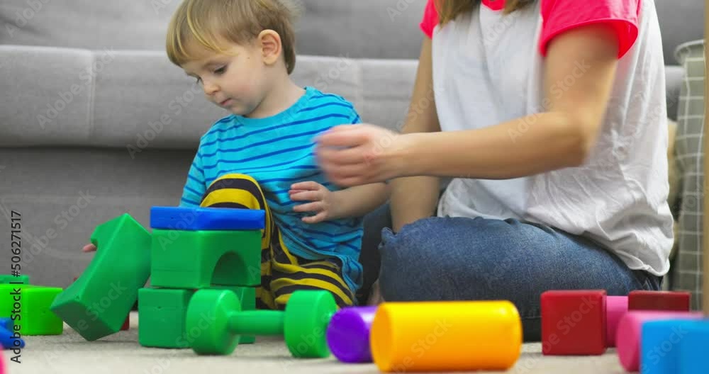 Mother with her son playing with colored cubes sitting on the floor at home. Family spends time together at home in children's room Mother with her son playing with colored cubes sitting on the floor at home. Family spends time together at home in children's room