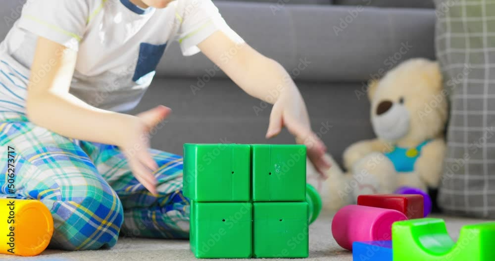 A child is playing with children building blocks on floor. Building a tower of cubes. Educational toys for children