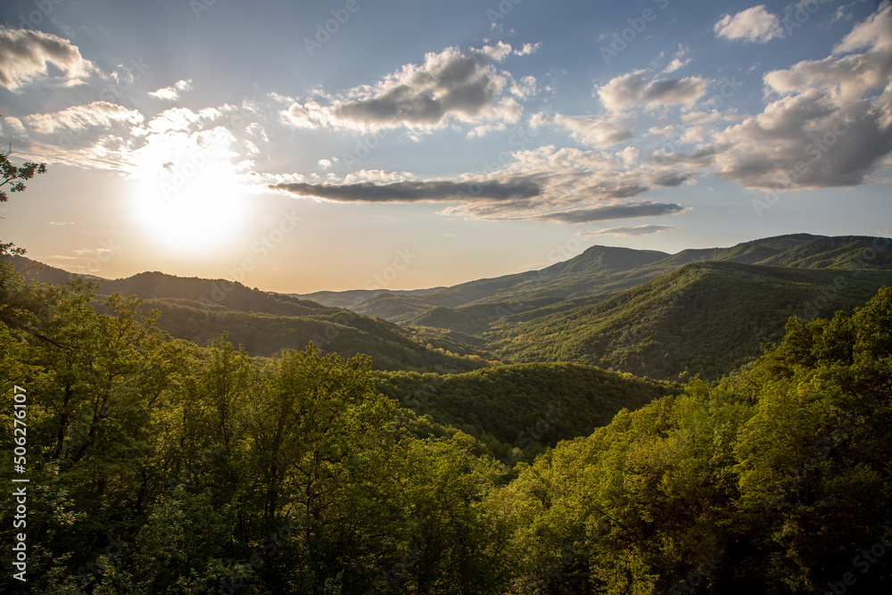 Beautiful mountains with green forest. The sun is setting in the sky. Colorful evening landscape. Beautiful nature.