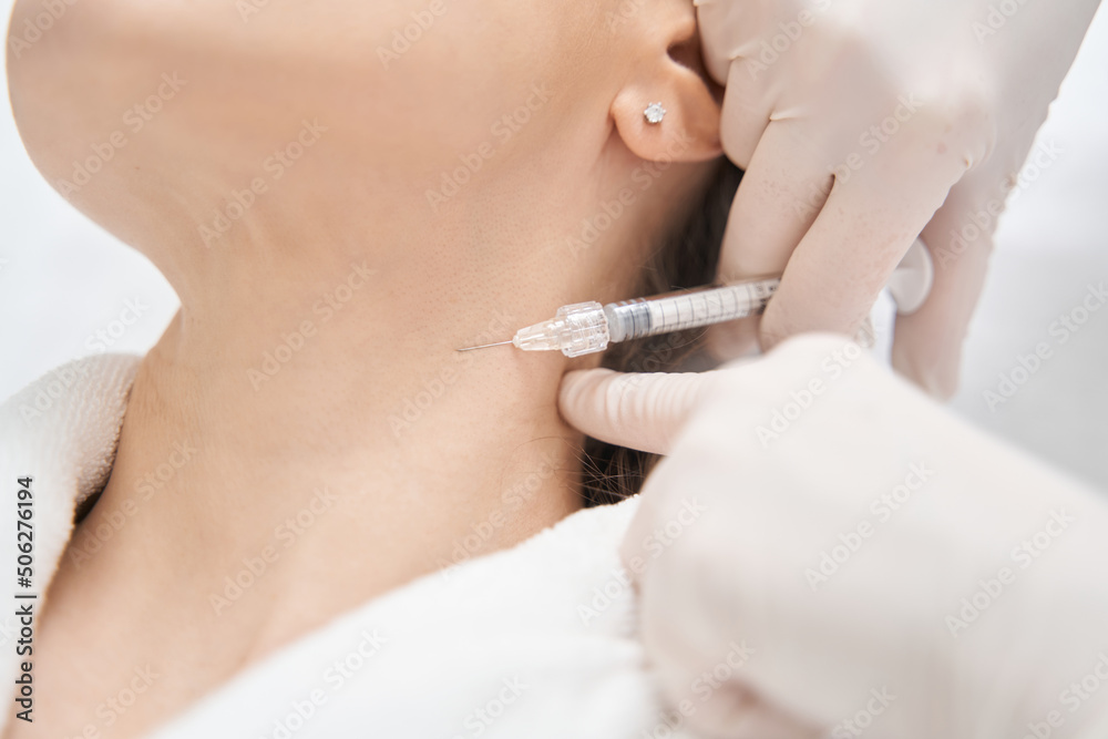 Doctor beautician doing injection into woman neck in beauty salon Doctor beautician doing injection into woman neck in beauty salon