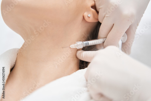 Doctor beautician doing injection into woman neck in beauty salon