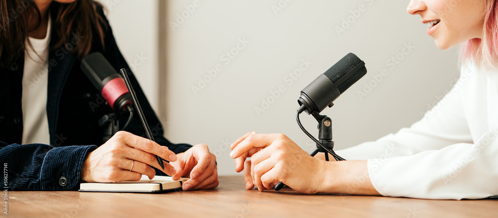 Naklejka premium Two woman hosts in local broadcat studio recording audio podcast, hands close-up, sitting opposite each other
