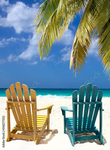 Beach chairs on a white sand coast under palm branch