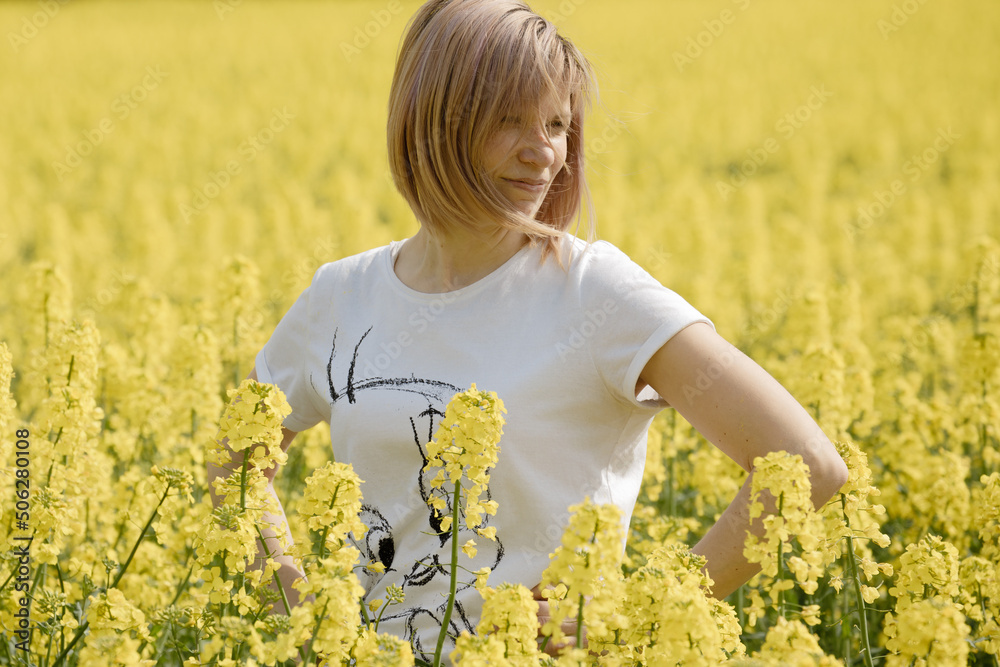 Fototapeta premium Woman in a flowering rape field. Rapeseed flowers yellow to sun. The farmer grows oilseed rape