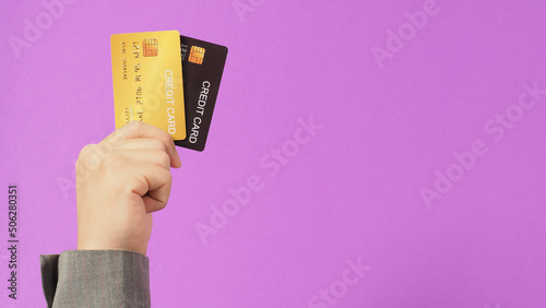 Hands are holding gold and black credit cards on purple background. Man arm wear a grey suit