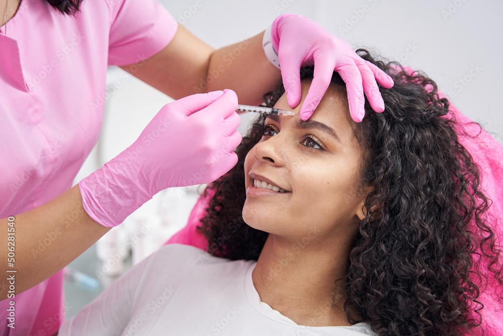Fototapeta premium Cosmetologist performs procedure for eliminating frown lines on patient face