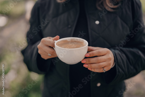 Female hands holding white porcelain cup of coffee. Fresh hot drink with foam from coffee-machine. Caffeine, energy, aroma concept