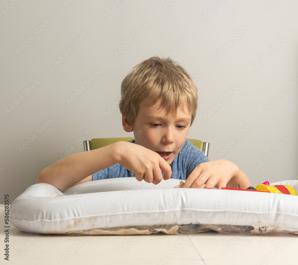 a boy with blond hair plays with sand in an inflatable sandbox for the house. a boy with blond hair plays with sand in an inflatable sandbox for the house.