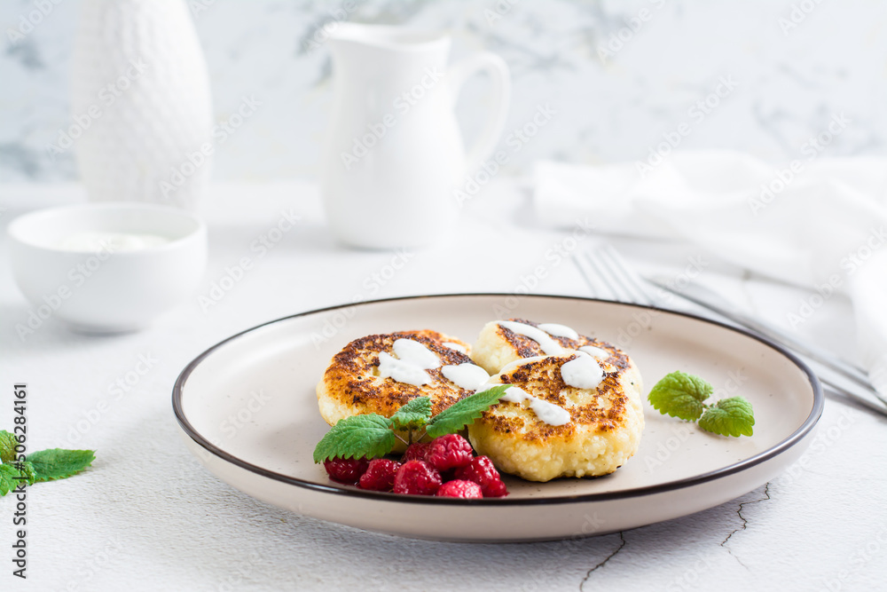 Cottage cheese pancakes with sour cream, raspberries and mint on a plate on the table. Copy space