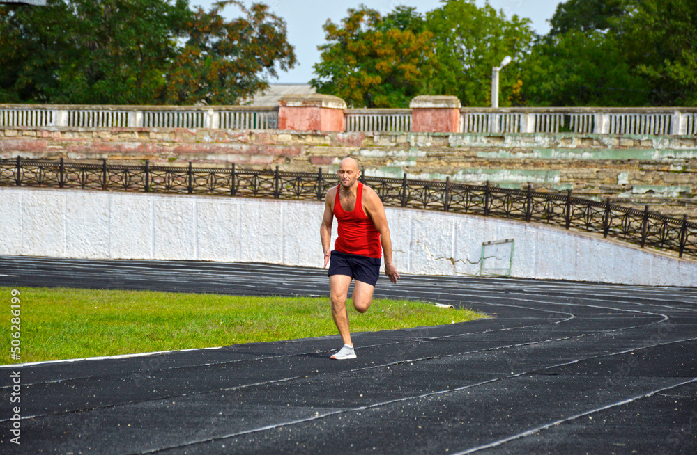 young muscular athlete runs on a black rubber treadmill in the stadium. outdoor training. active lifestyle and sports