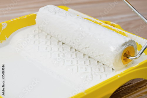 Painting apartment, renovating with white color paint. Paint roller in paint tray with white color in the tray on brown paper