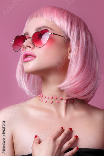 Close-up portrait of woman in sunglasses with bright colored pink hair and make-up on pink.