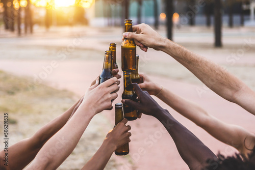 Group of multiracial young friends having fun celebrating together while cheering with beer bottles at summer party on vacation