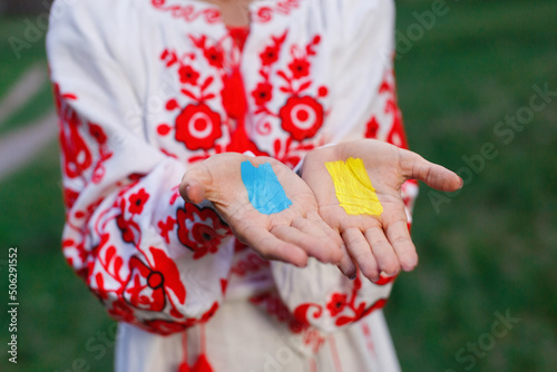 Ukrainian woman in embroidered white and red shirt close up outdoor portrait. hands with ukraine blue and yellow flag on palms on background. Stop the war in Ukraine concept. No war. help ukraine
