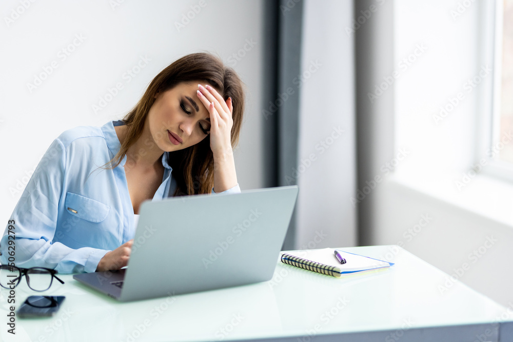 Young attractive woman at modern office desk, working on laptop, massaging temples to forget about constant headaches, noisy loud office giving a migraine, relieving stress, chronic pain, help soothe Young attractive woman at modern office desk, working on laptop, massaging temples to forget about constant headaches, noisy loud office giving a migraine, relieving stress, chronic pain, help soothe