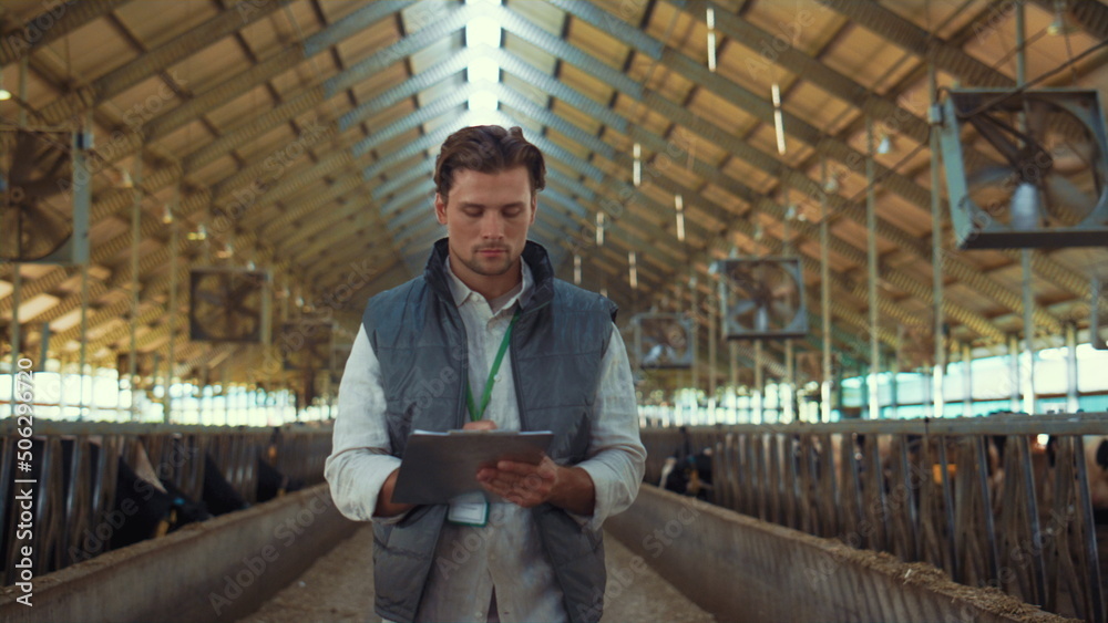 Livestock owner checking animal feedlots making notes on clipboard at cowshed. - obrazy, fototapety, plakaty 