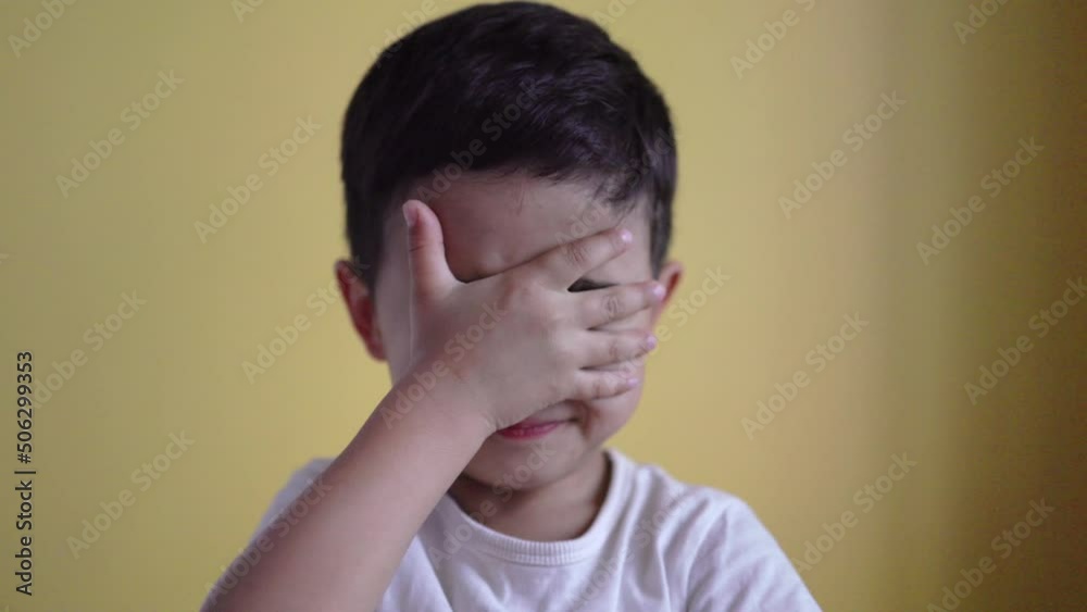Cute boy smiling and covering his face on colour background Cute boy smiling and covering his face on colour background
