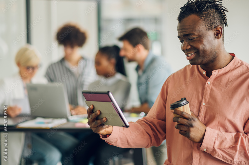 Black business man using tablet in the office with his team working in the back Black business man using tablet in the office with his team working in the back