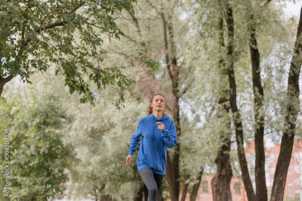a European woman in a blue hoodie is running and doing sports in the park. selective focus, fitness and yoga outdoor sports, exercise and meditation and fitness for body health. spiritual development
