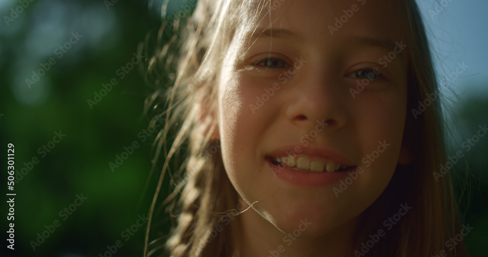 Fototapeta premium Cheerful blond girl posing in golden sunlight. Playful child looking in camera 