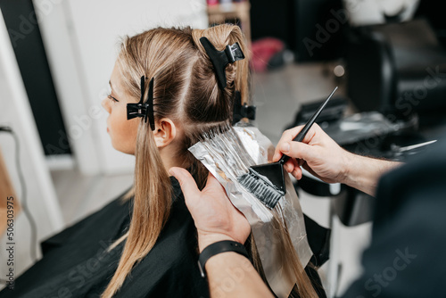 Hairdresser is applying bleaching powder on woman\'s hair and wrapping into the foil.