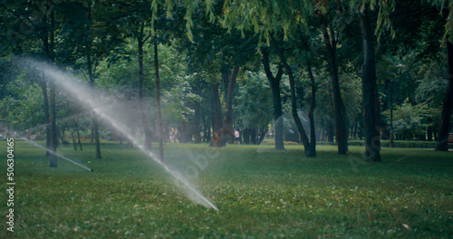 Automatic sprinklers system watering green lawn on sunny summer day at park.