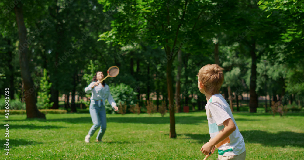 Active boy playing badminton with mother back view. Sport in family life concept Active boy playing badminton with mother back view. Sport in family life concept