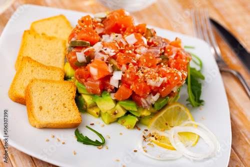 Gourmet salmon tartare with chopped avocado and toasted bread served on white plate