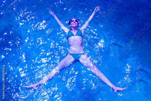 woman in a swimsuit floats on blue ocean water, photographed from above