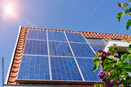 Solar panel on a red roof reflecting the sun and the cloudless blue sky photo