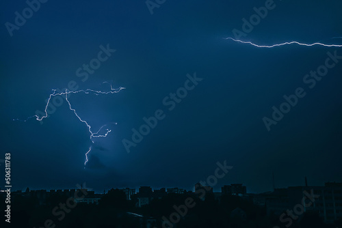 Lightning in sky over city. Bright flashes on dark night. Thunderclouds and electricity discharges in atmosphere. Night cityscape.