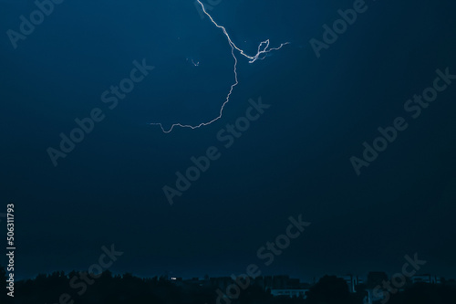 Lightning in sky over city. Bright flashes on dark night. Thunderclouds and electricity discharges in atmosphere.